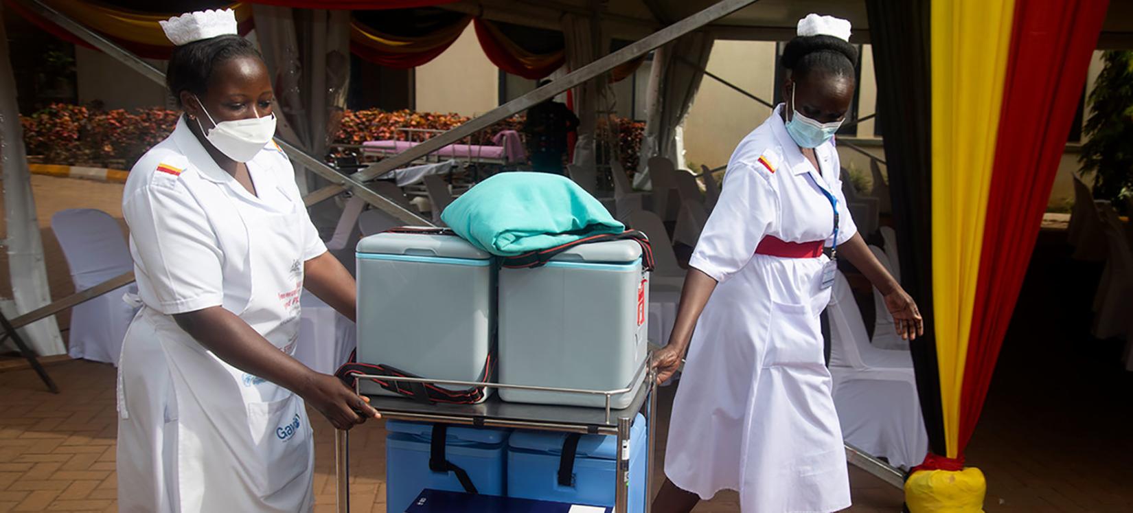 Two health workers carrying a trolley of vaccines.