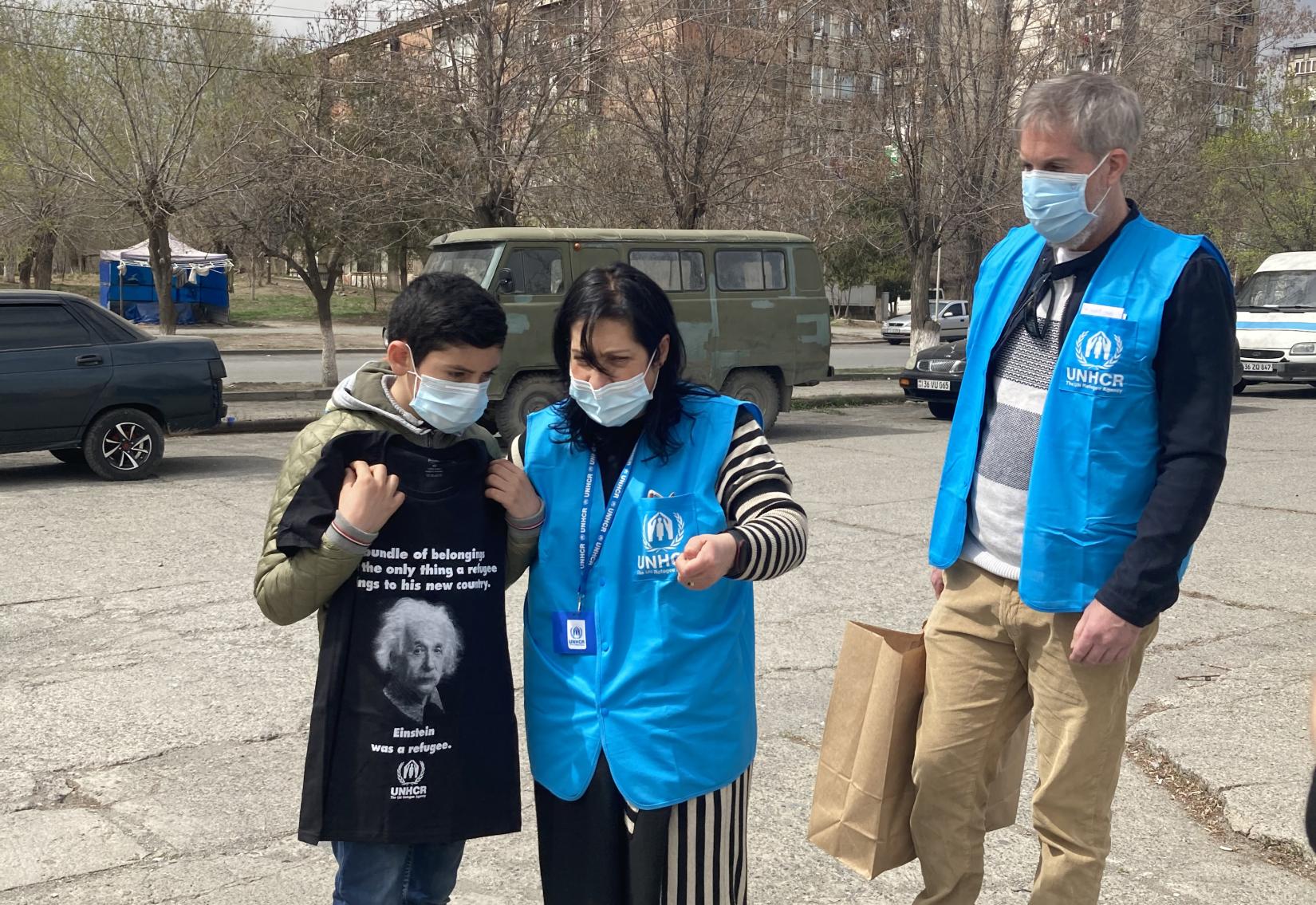 UNHCR staff members give a UNHCR T-shirt to a young boy