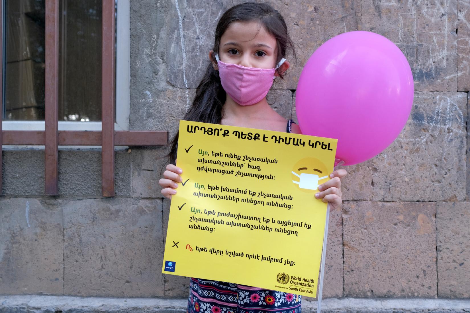 Little girl holding a COVID19 poster and wearing a mask.