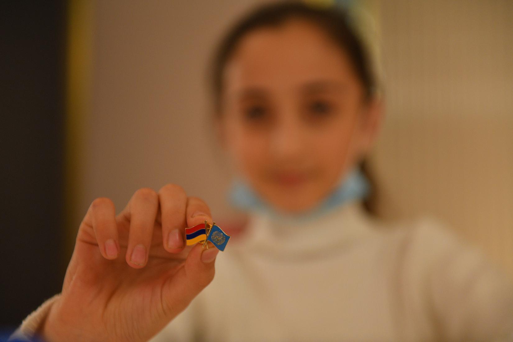 A girl shows the pin with UN's and Armenia's flags.