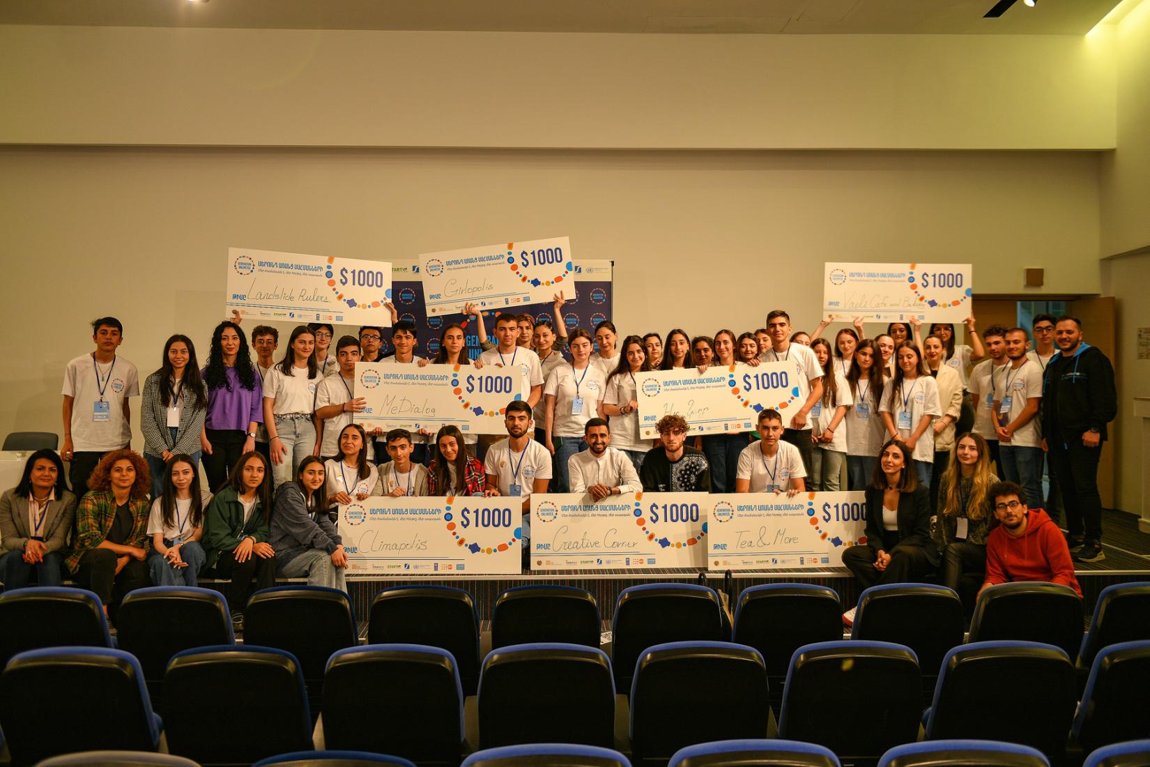 Lots of happy Armenian startup teams of adolescents on the stage holding their prize.