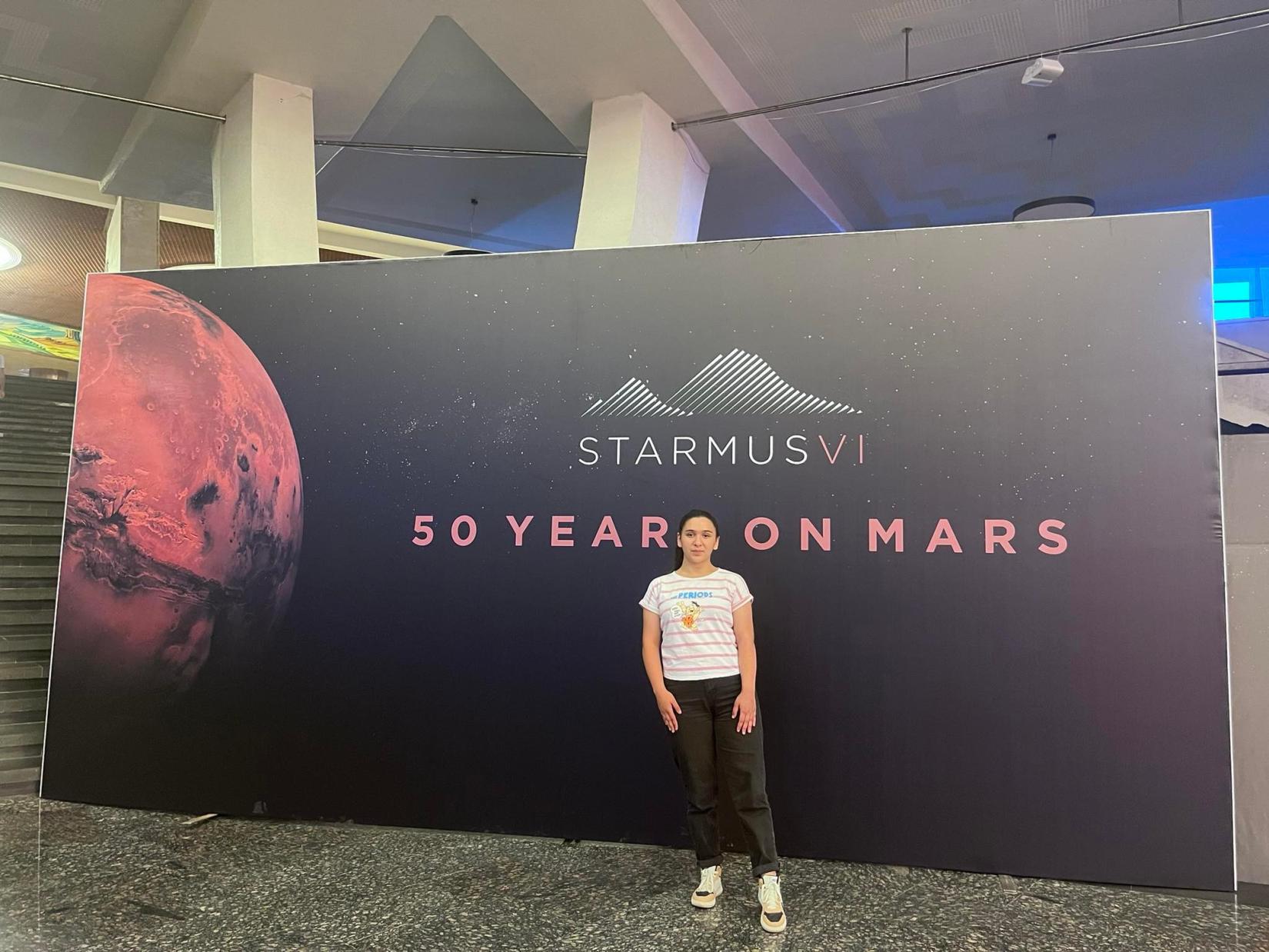 A teenager standing next to the STARMUS VI Armenia festival poster.