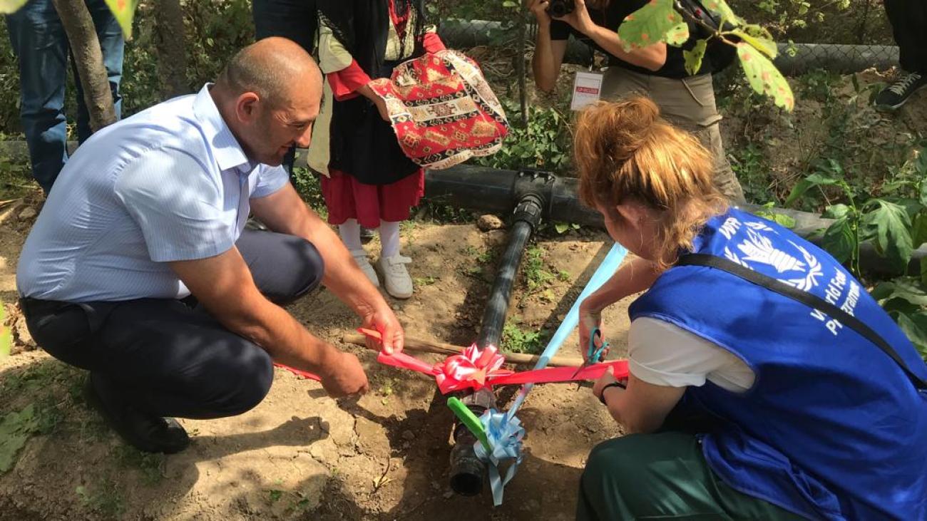 A woman and a man cut the red ribbon attached to the water line, marking the beginning of irrigation.
