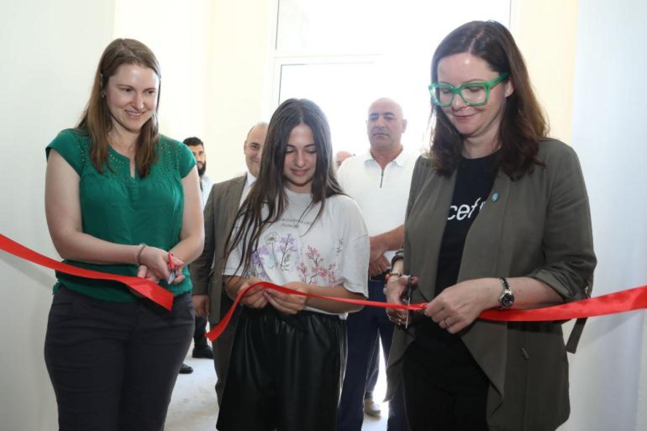 Two adults and a girl cutting the red ribbon at the child-friendly center in Aghavnadzor.