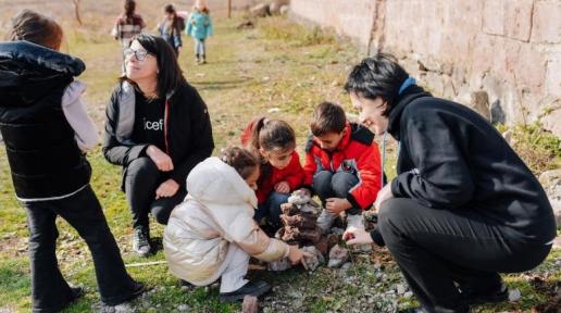 Two women playing with four kids. Three other kids are walking.