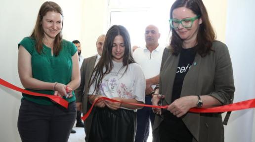 Two adults and a girl cutting the red ribbon at the child-friendly center in Aghavnadzor.